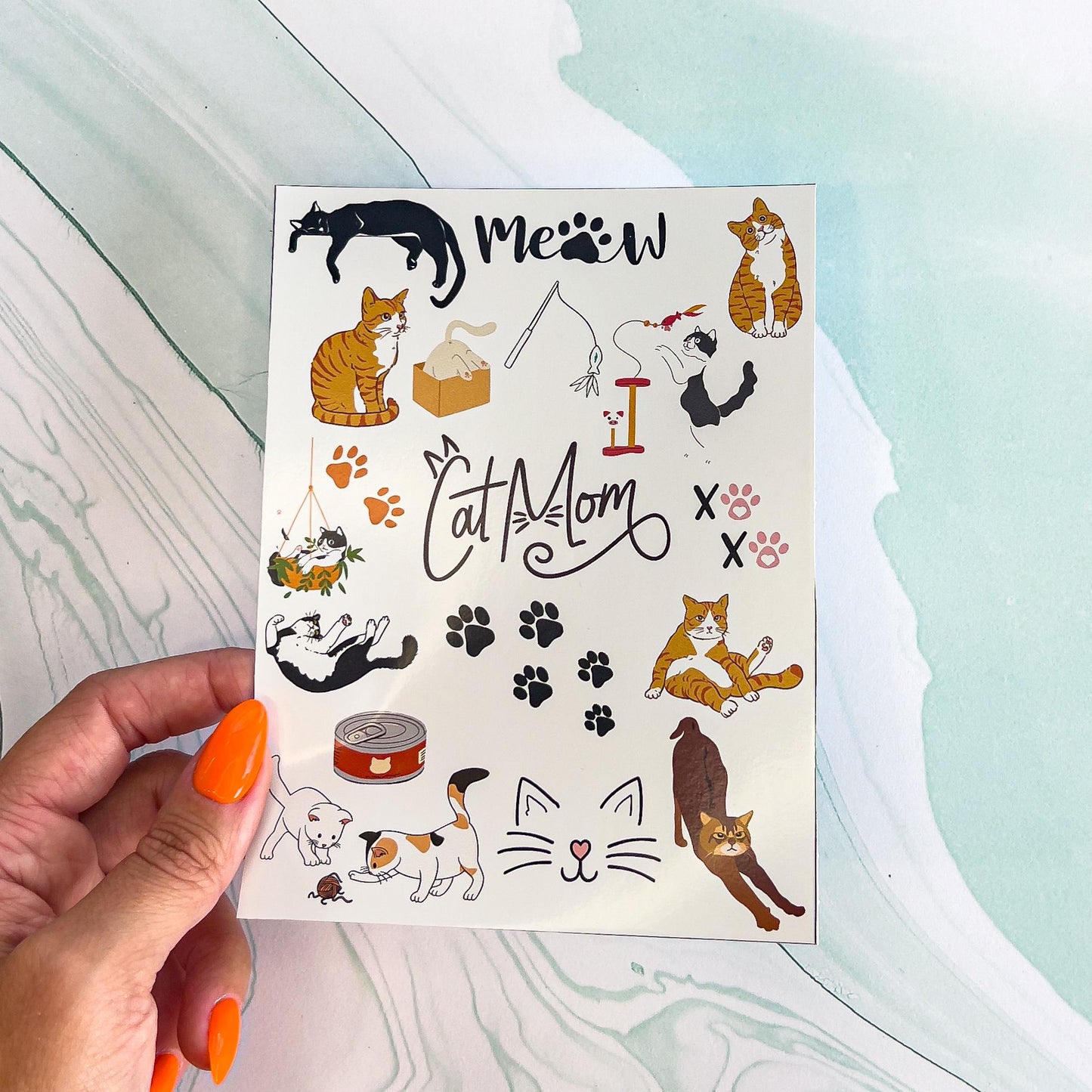 A sheet of various cat themed stickers. The stickers include cats in various colors and poses, canned cat food, cat toys, cat tree, paw prints, the words "CAT MOM" with cat ears and whiskers and "MEOW" with a paw print instead of an "O", a cat in a box, two kittens playing, and "XO XO" with paw prints instead of the "O"