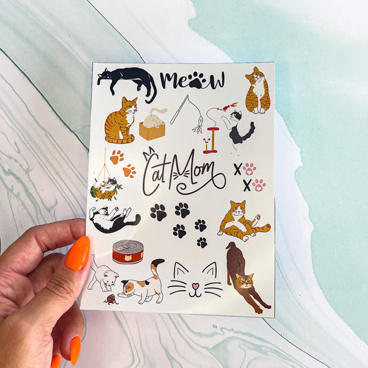 A sheet of various cat themed stickers. The stickers include cats in various colors and poses, canned cat food, cat toys, cat tree, paw prints, the words "CAT MOM" with cat ears and whiskers and "MEOW" with a paw print instead of an "O", a cat in a box, two kittens playing, and "XO XO" with paw prints instead of the "O"