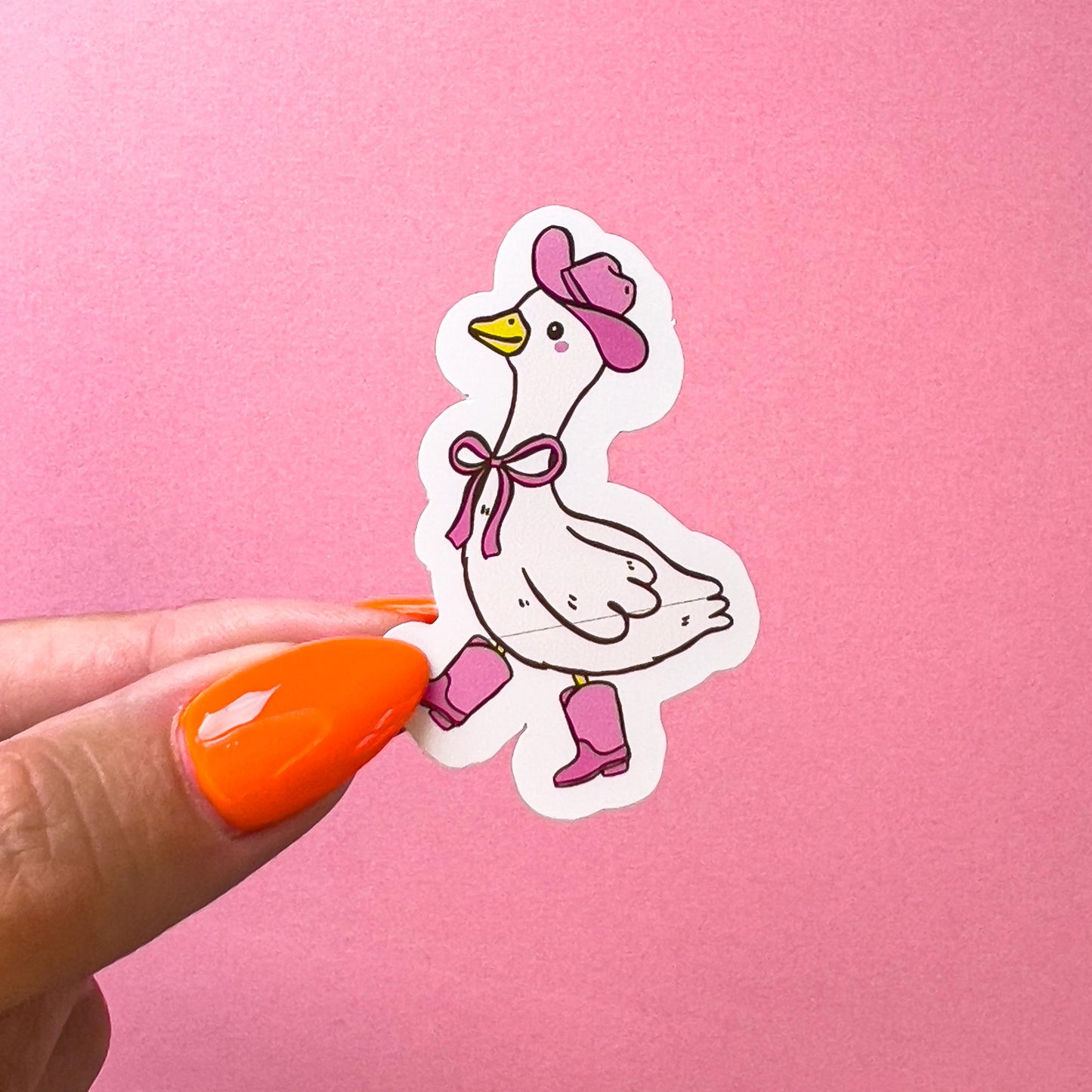 A vinyl decal sticker of a cowboy/western themed goose/duck. The goose/duck is wearing a pink cowboy hat, pink cowboy boots, and a pink bow around its neck. The goose/duck has a yellow beak and is in a walking stance. The goose/duck has pink blushed cheeks.