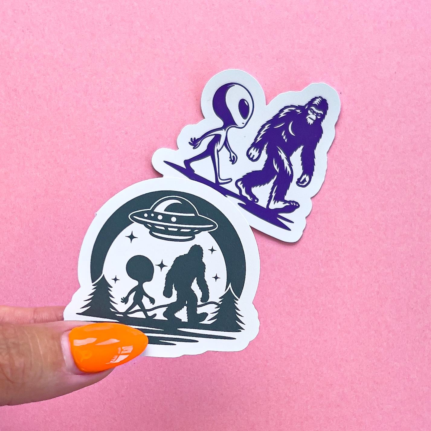 Two viny decal stickers featuring big foot and an alien.