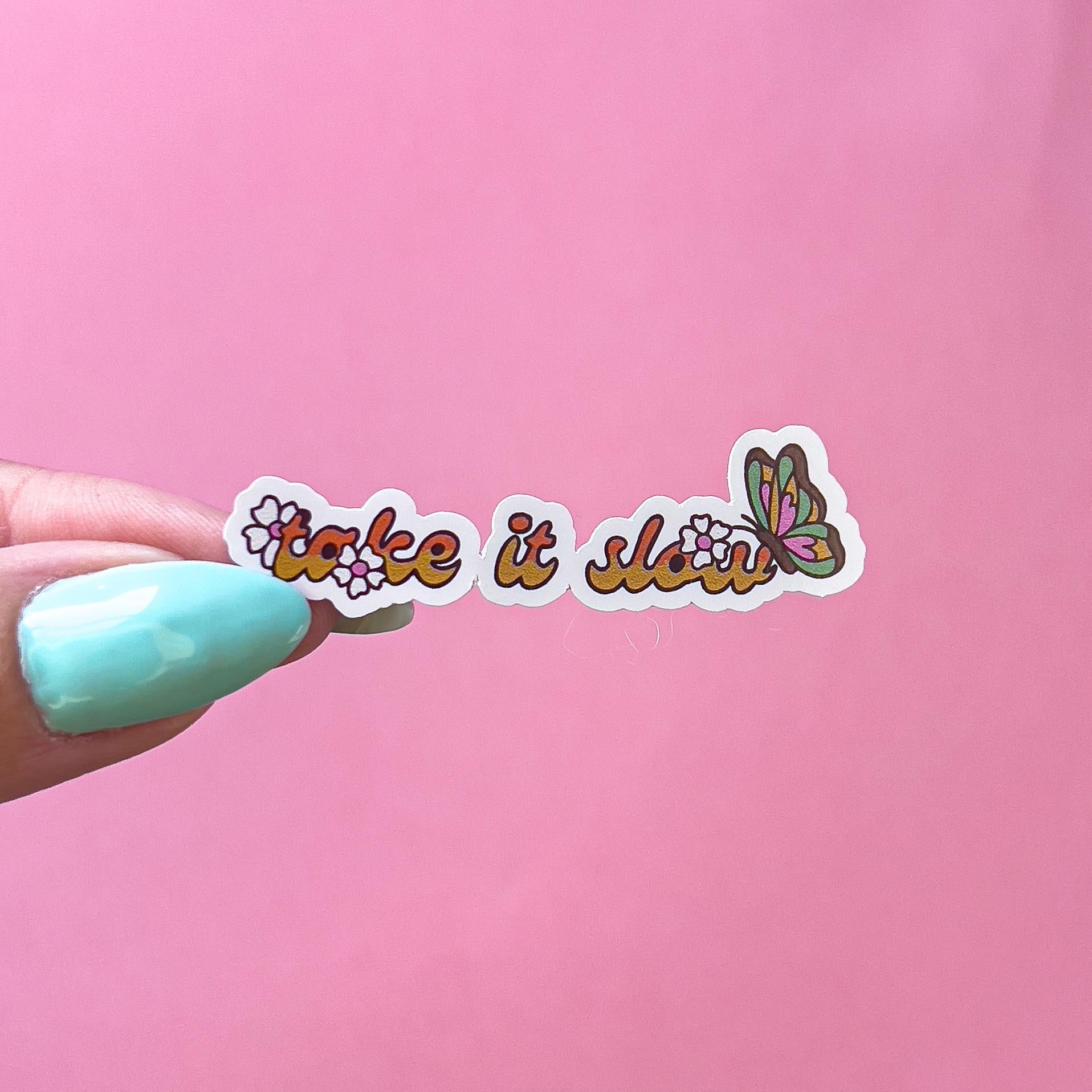 A vinyl decal sticker with orange and yellow text that reads 'take it slow' with a butterfly and flowers on the text.