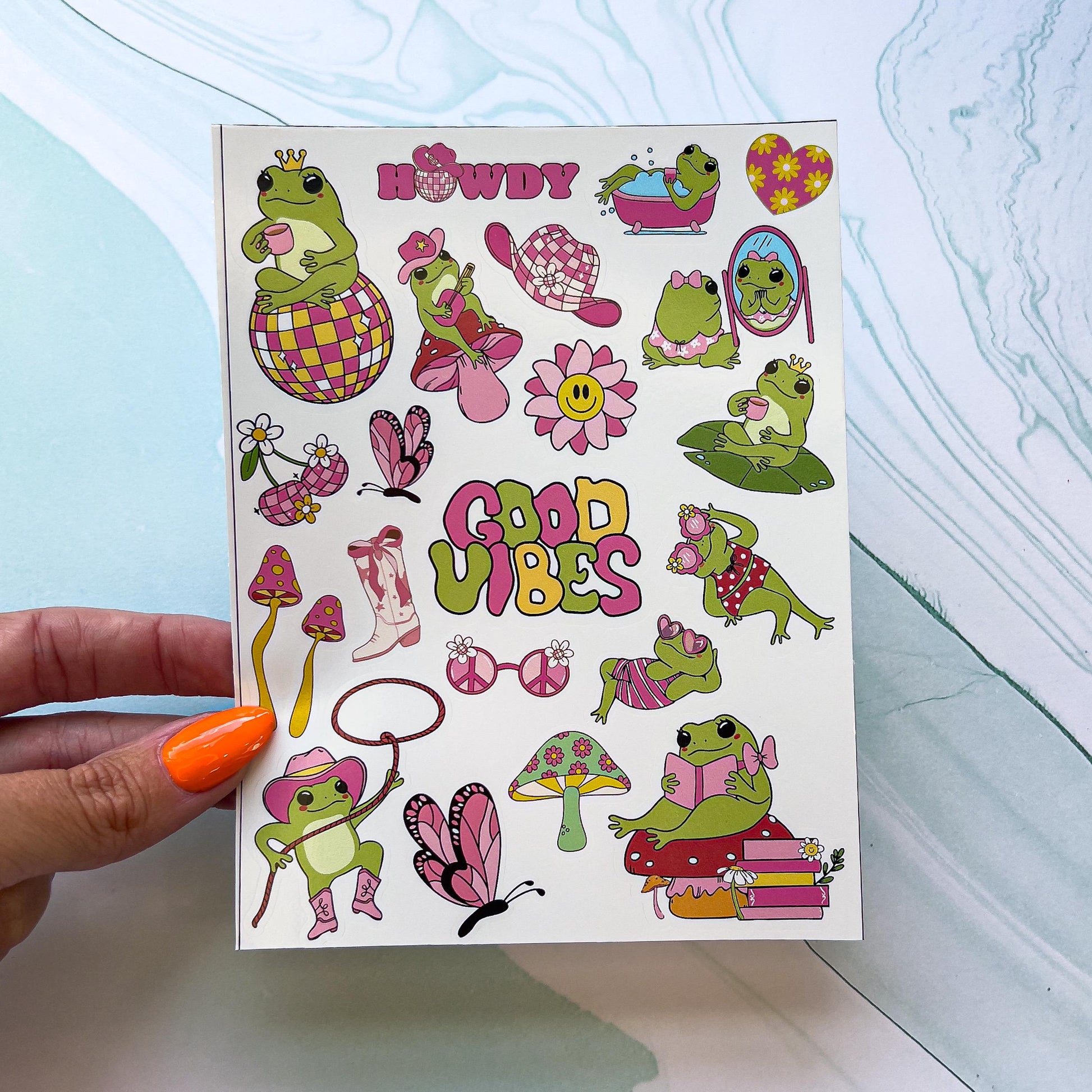 A sheet of stickers featuring frogs in various outfits and poses. The stickers include a cowboy frog with a lasso, a frog on a stack of books with a bow, frogs in swimsuits and heart shaped sunglasses, a frog wearing a crown while sitting on a disco ball, a cowboy frog playing guitar , a pink cowboy hat, butterflies, mushroom, cowboy boots, "GOOD VIBES", "HOWDY" with a cowboy hat on a disco ball instead of an "O", ect. The stickers are shades green, pink, and yellow.