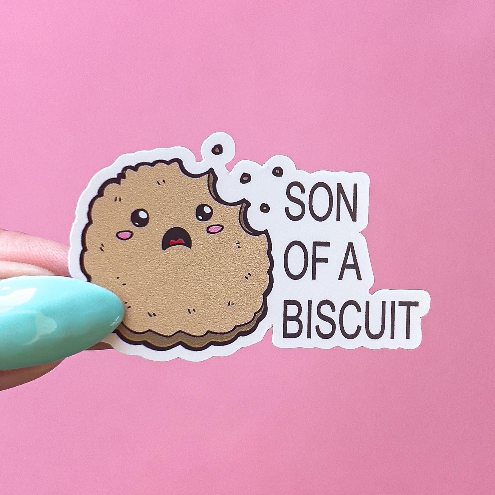 A vinyl decal sticker with a brown cartoon biscuit with a bite taken out of it. The biscuit has a surprised expression with open mouth and blushed cheeks. The text on the sticker reads 'SON OF A BISCUIT'.